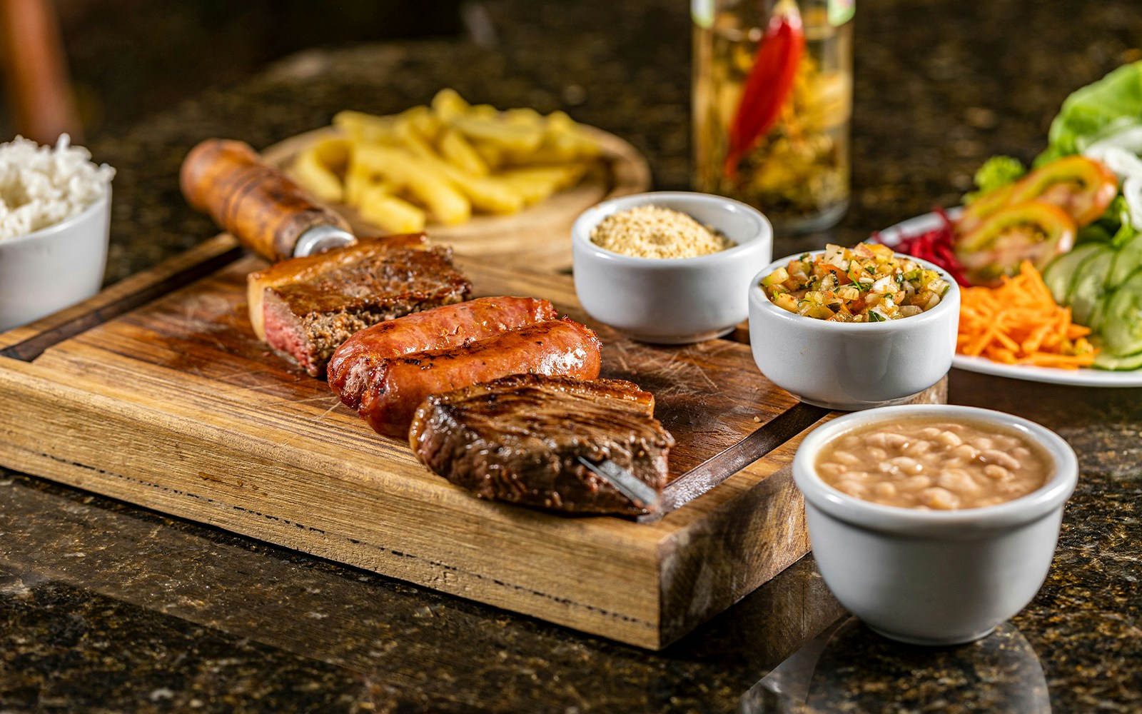 Brazilian barbecue with grilled meats, rice, beans, and sides on a wooden board.