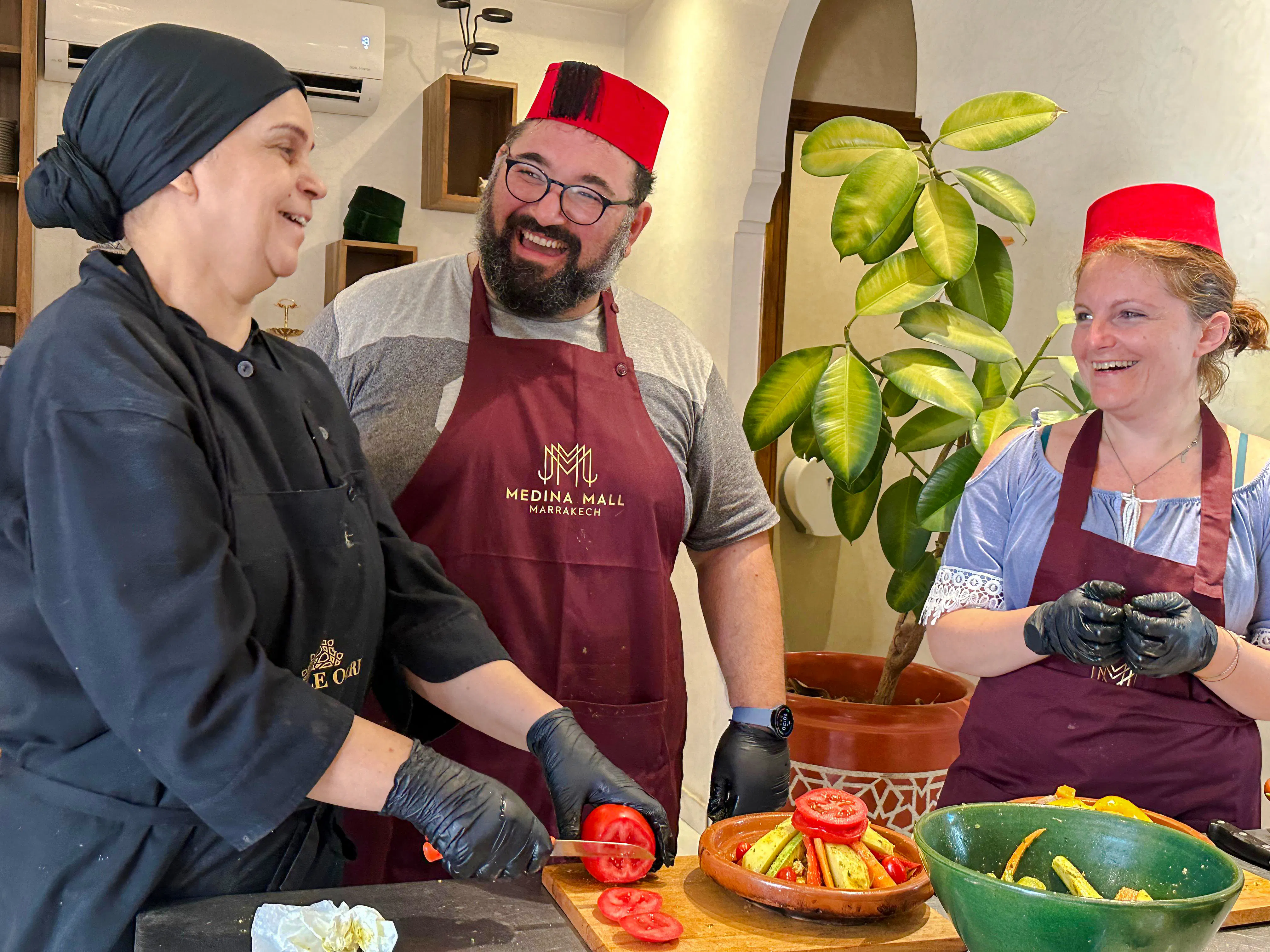 Local chef teaching tagine cooking class in Marrakech with participants wearing aprons and hats.