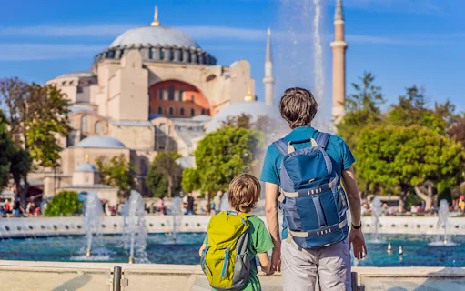 Tourists with backpacks viewing Hagia Sophia, Istanbul, near a fountain.