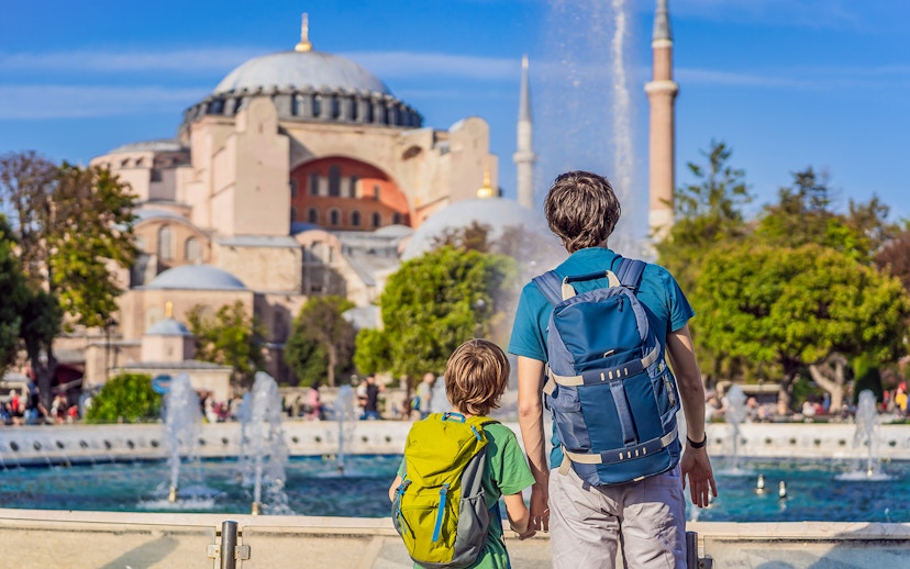 Tourists with backpacks viewing Hagia Sophia, Istanbul, near a fountain.