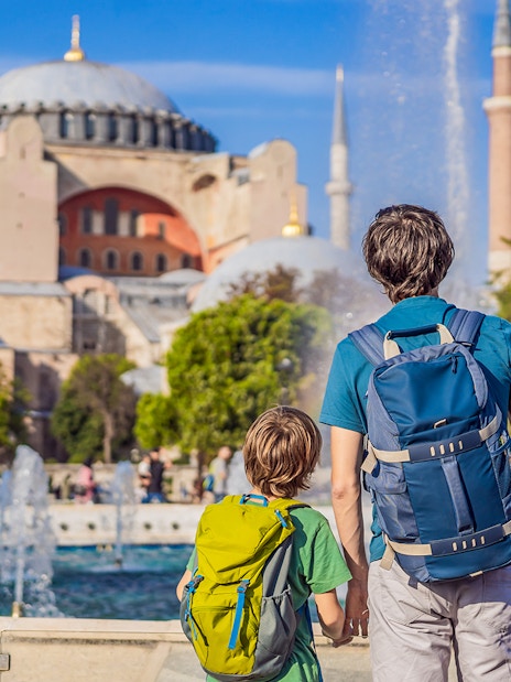 Tourists with backpacks viewing Hagia Sophia, Istanbul, near a fountain.