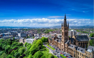 University of Glasgow main building with cityscape and greenery, part of self-guided exploration game.