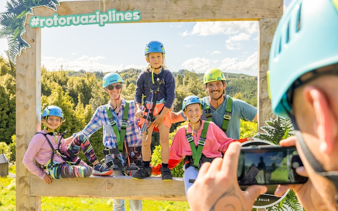 Group posing at Rotorua Ziplines with helmets and harnesses, surrounded by lush forest.