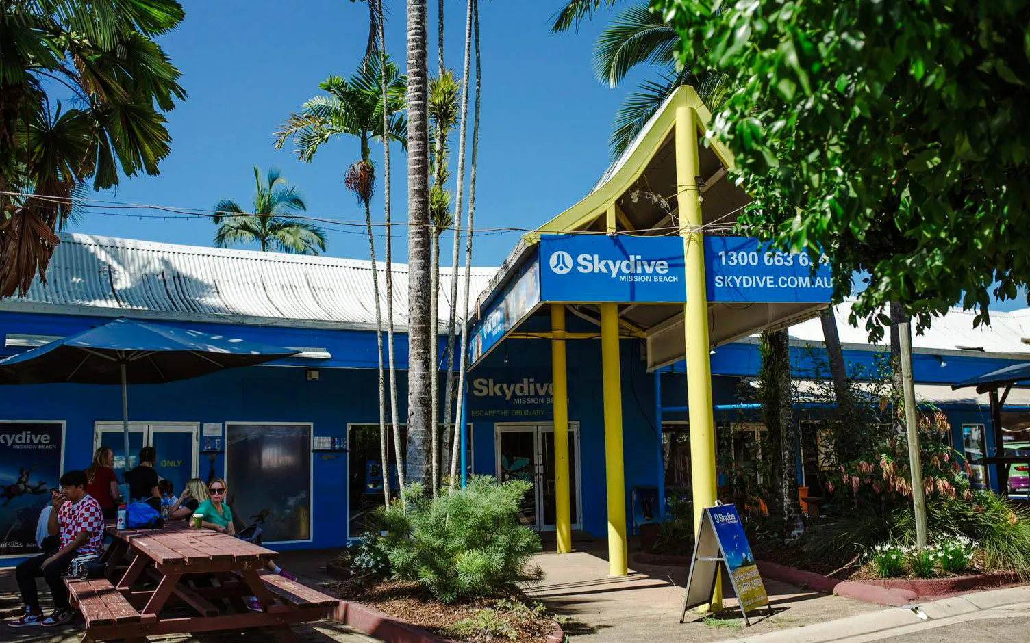 Skydive Mission Beach entrance with people seated outside under palm trees.