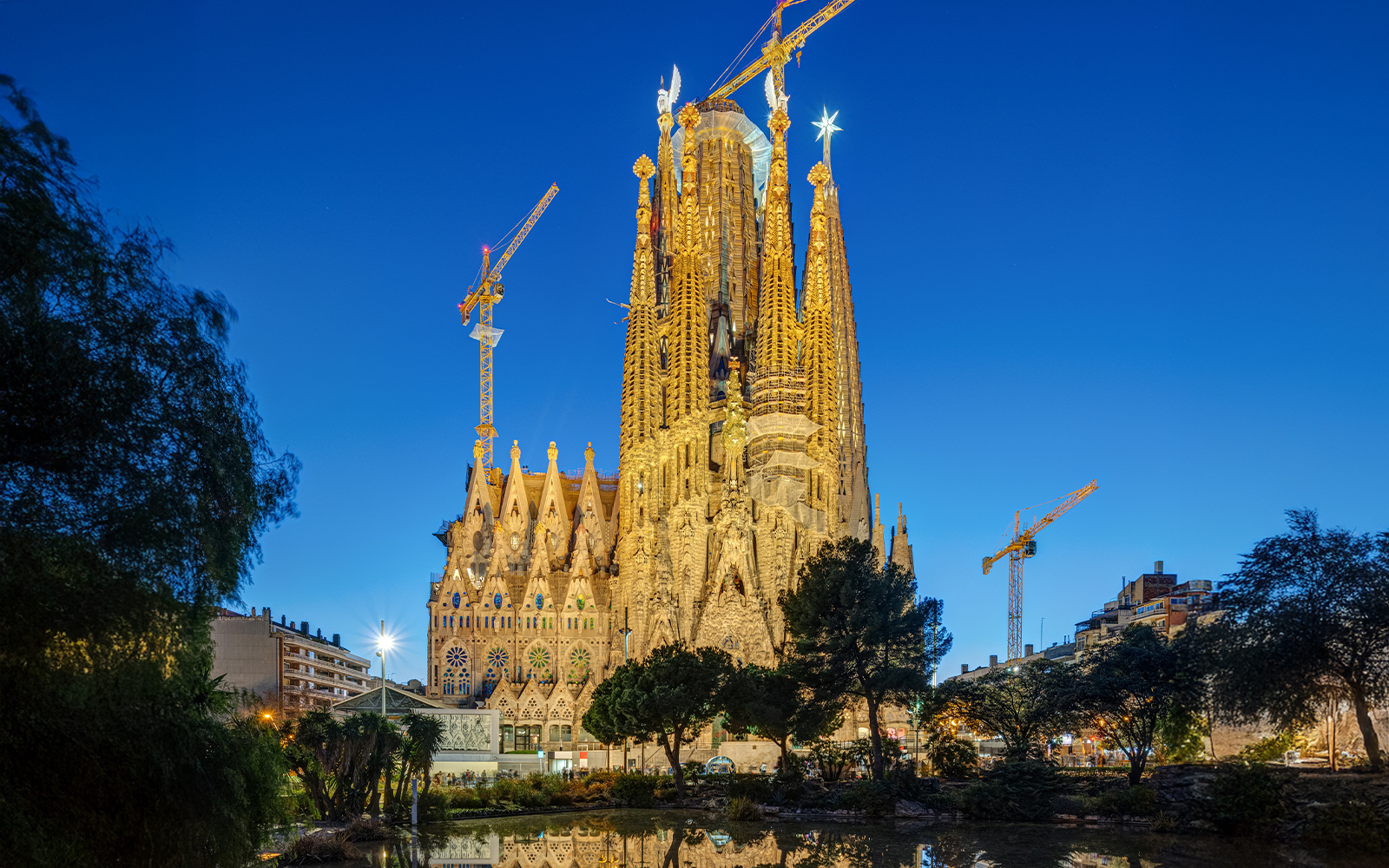 Sagrada Familia in Barcelona illuminated during blue hour with cranes visible.