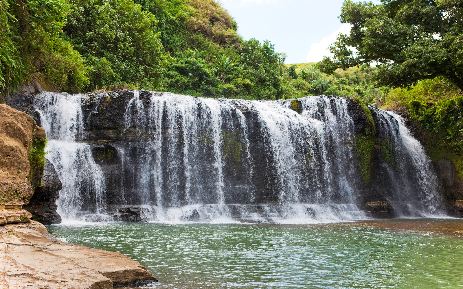 Talofofo Falls Park waterfall cascading over rocks surrounded by lush greenery in Guam.