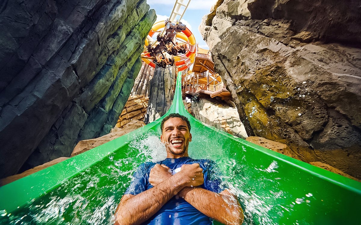 Person enjoying a thrilling water slide at Jabel Drop, surrounded by rocky cliffs.