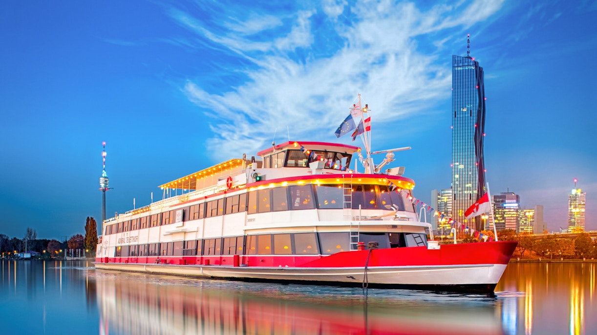 River cruise ship on the Danube River in Vienna, Austria, with city skyline in the background.