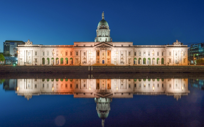 Parliament House in Dublin illuminated at night, reflecting in the river.