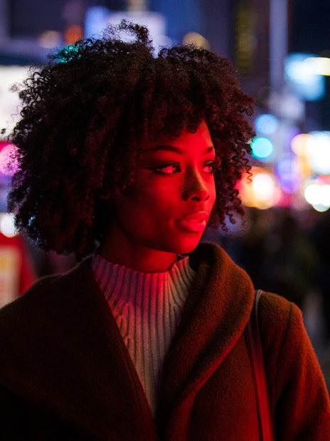 Woman standing in Times Square at night with colorful lights in the background.