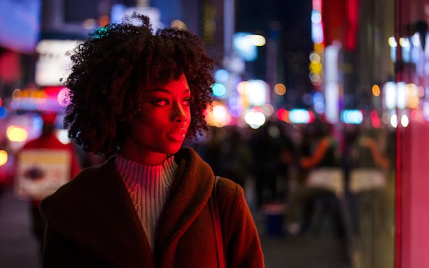 Woman standing in Times Square at night with colorful lights in the background.