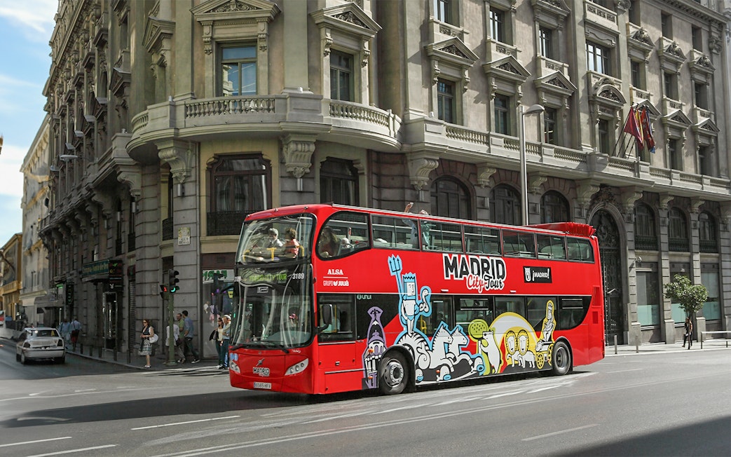 Red double-decker bus on Madrid city tour passing historic buildings.