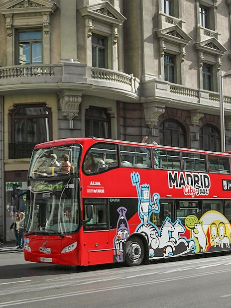 Red double-decker bus on Madrid city tour passing historic buildings.