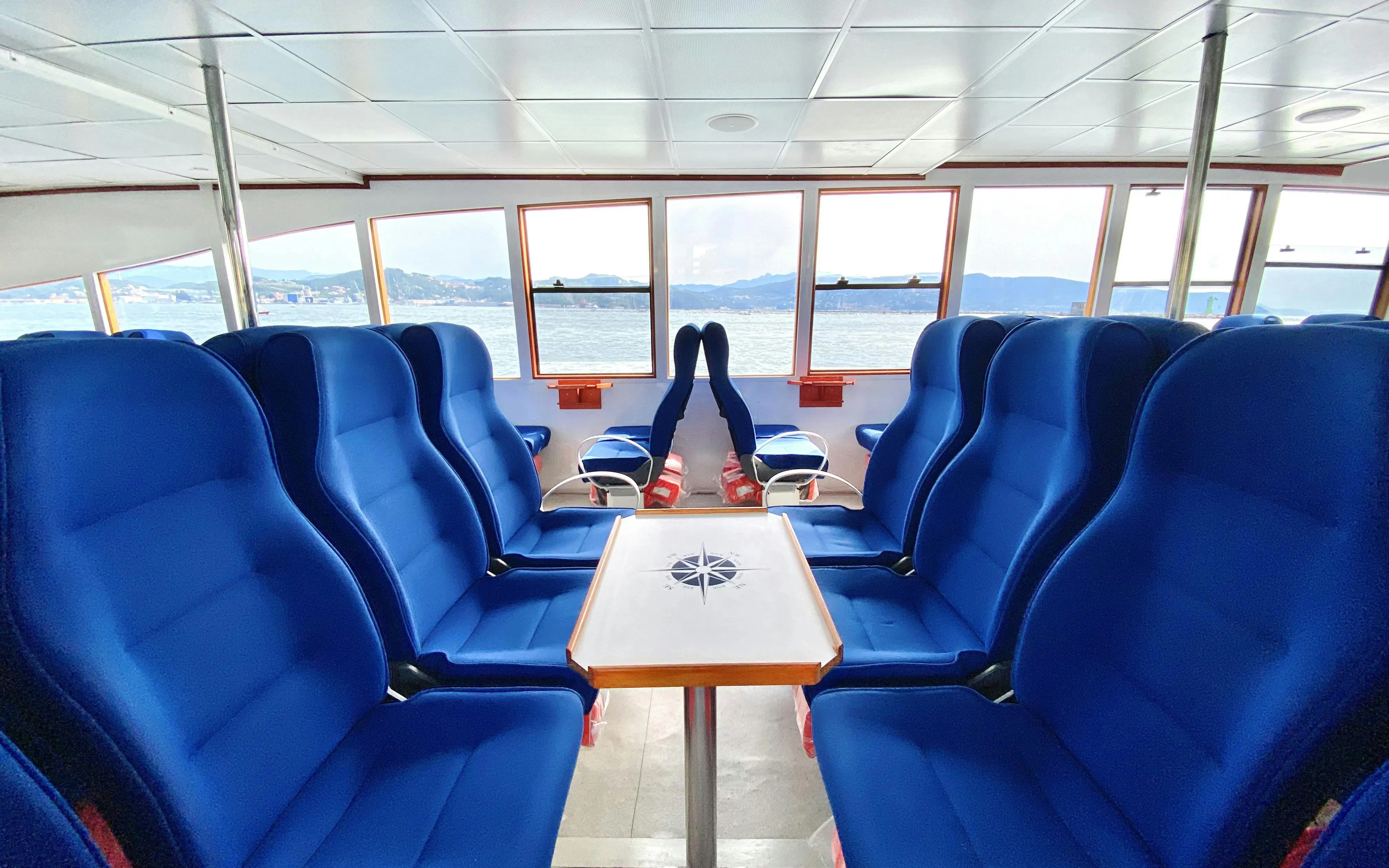 Interior seating area on a Cinque Terre cruise ship with ocean view through windows.