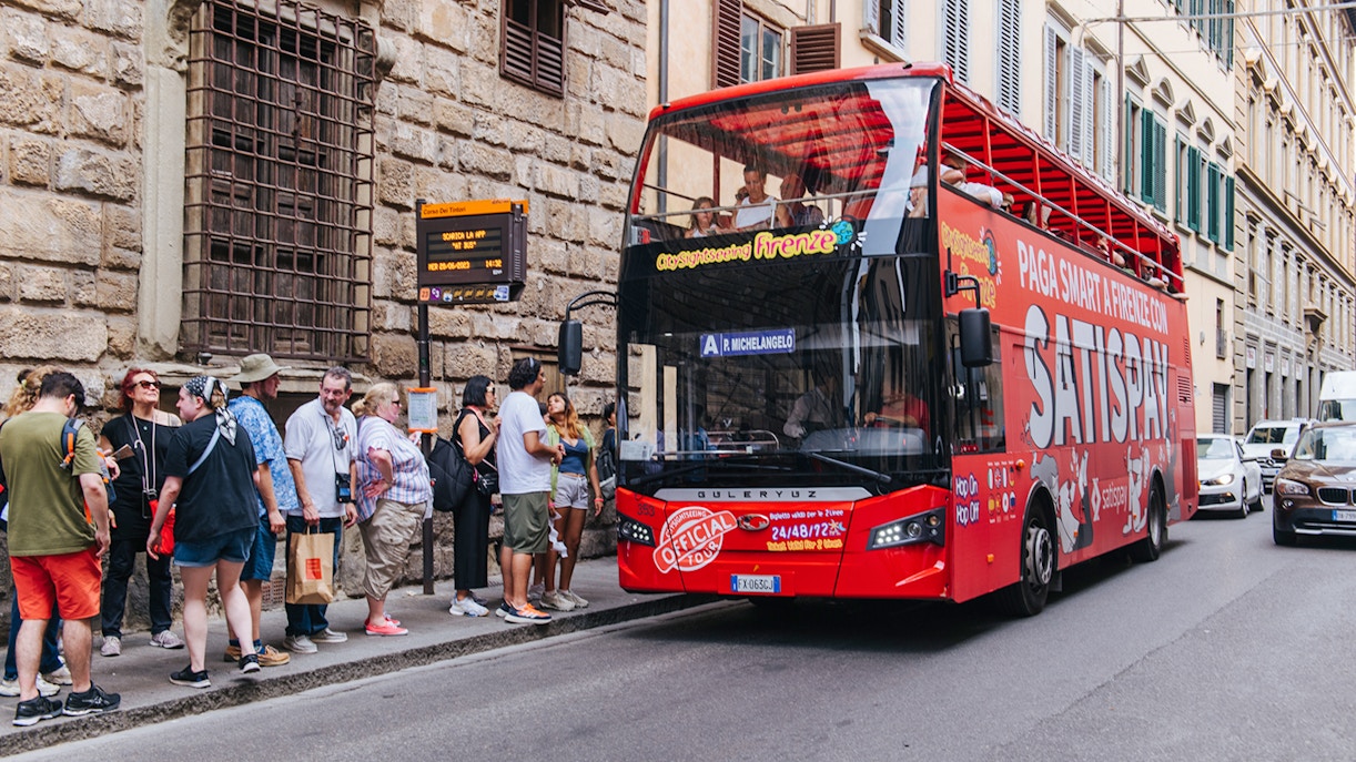 Tour guide showing a group of tourists around the Accademia Gallery in Florence, Italy, with a City Sightseeing Hop-On Hop-Off bus waiting outside for the next part of the Combo tour