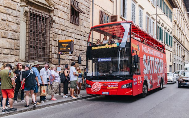 Tourists boarding a red sightseeing bus in Florence, Italy.