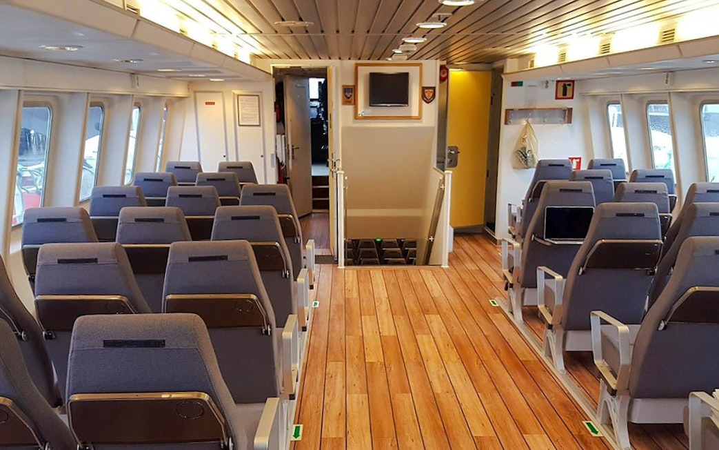 Inside seating area of a whale watching tour boat with rows of chairs and large windows.
