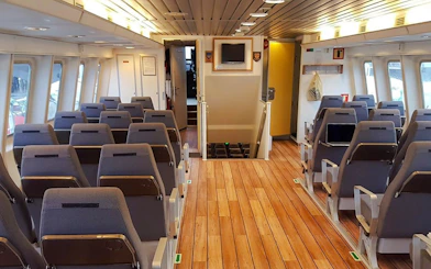 Inside seating area of a whale watching tour boat with rows of chairs and large windows.