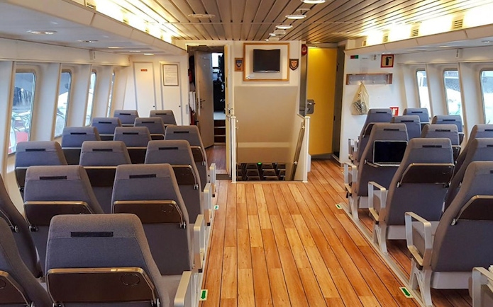Inside seating area of a whale watching tour boat with rows of chairs and large windows.