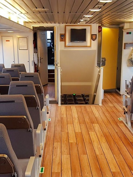 Inside seating area of a whale watching tour boat with rows of chairs and large windows.