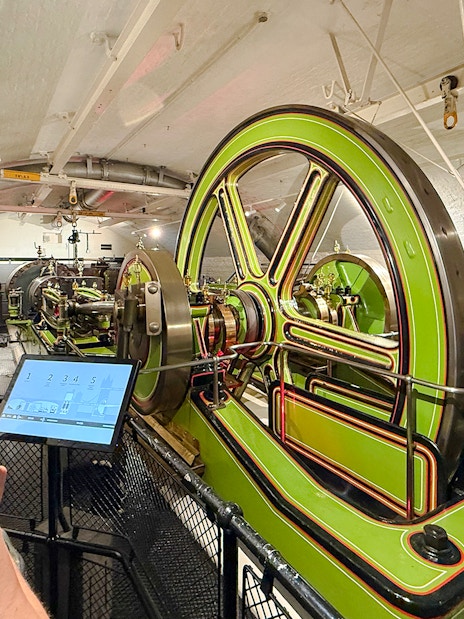 Tower Bridge engine room with green machinery and visitors exploring.