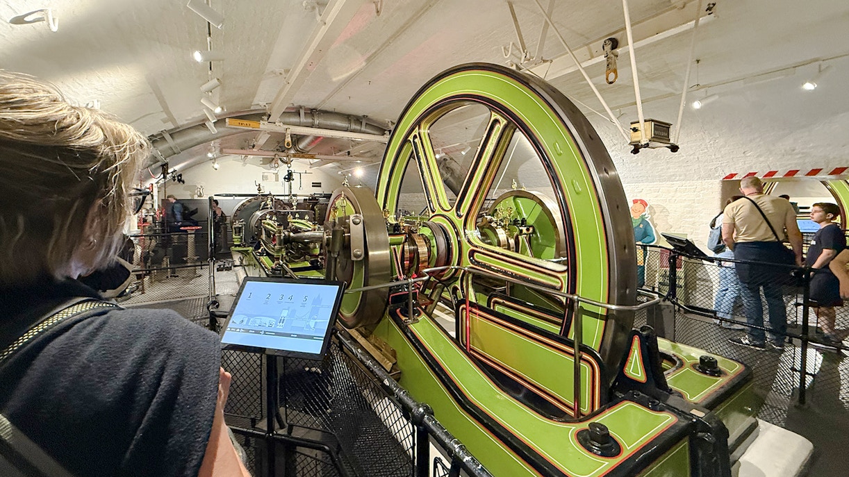 Tower Bridge engine room with green machinery and visitors exploring.