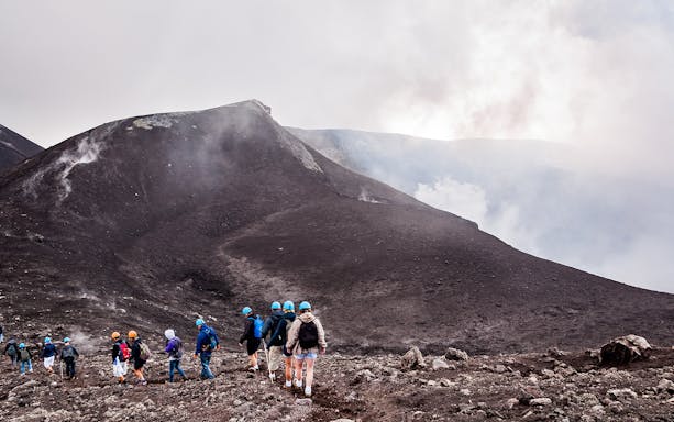 Hikers with helmets walking on Mount Etna's volcanic terrain.