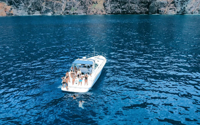 Boat with tourists on dolphin and whale watching tour near Calheta cliffs.