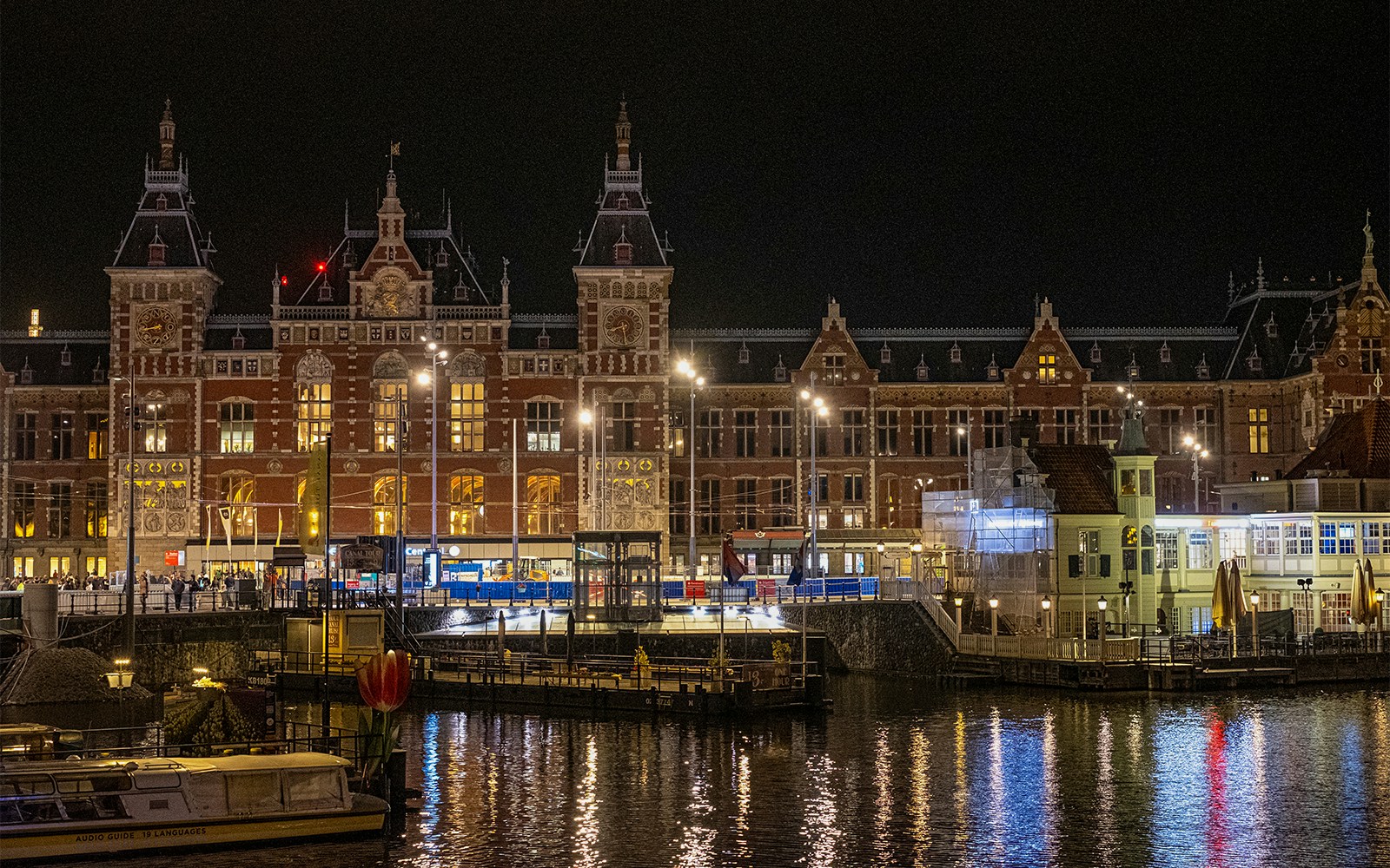Amsterdam Central Station illuminated at night, reflecting on the canal.