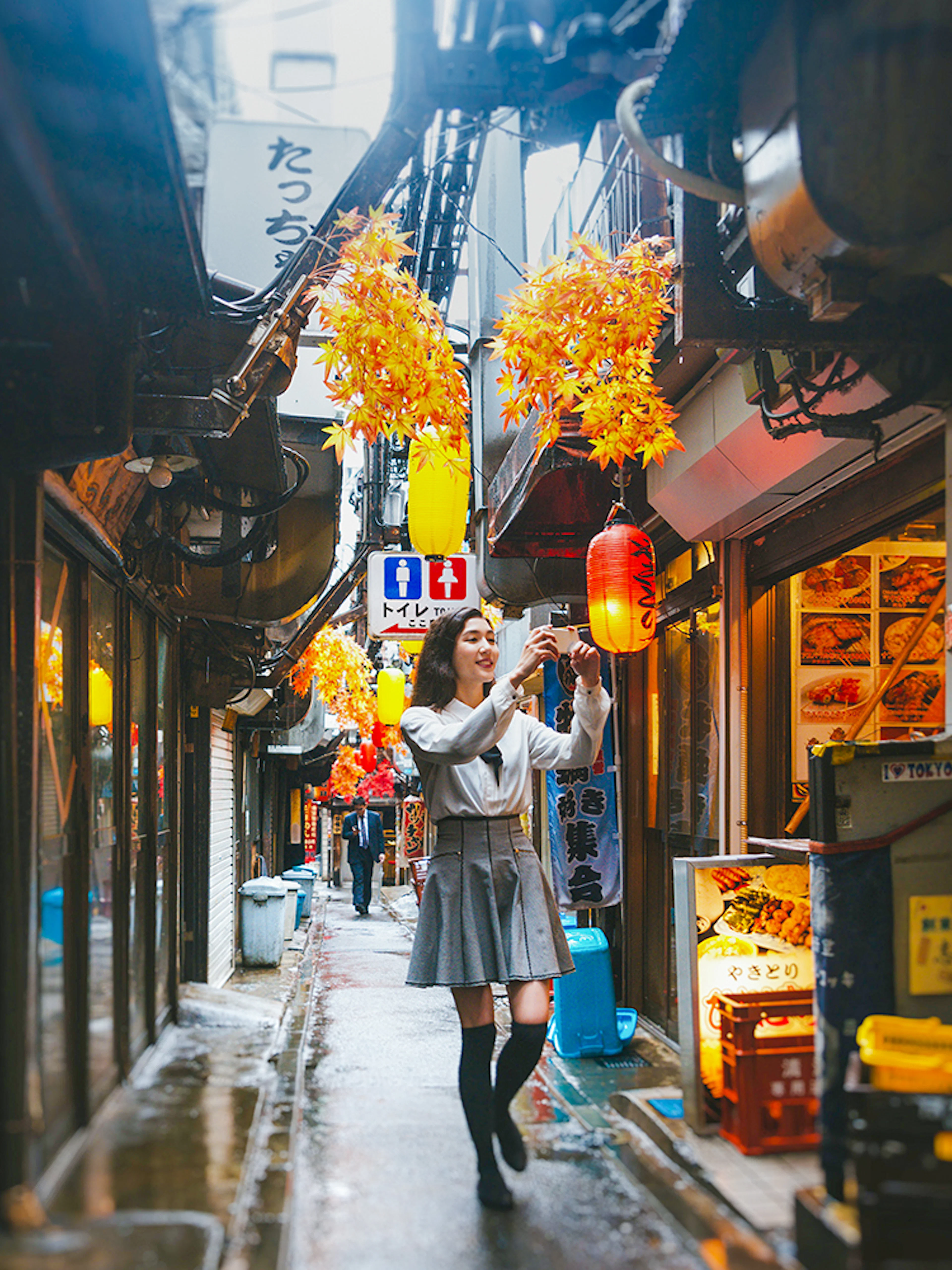 Lady taking photos in Golden Gai, Tokyo alley with lanterns and signs.
