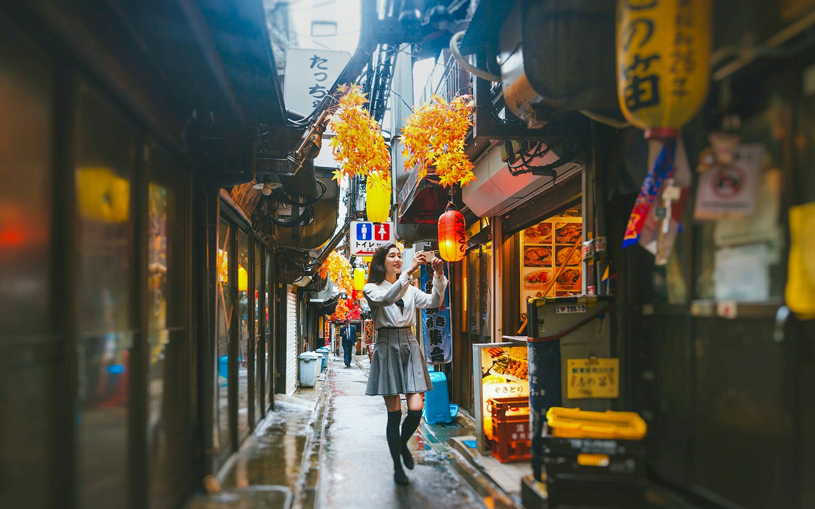 Lady taking photos in Golden Gai, Tokyo alley with lanterns and signs.