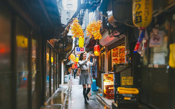 Lady taking photos in Golden Gai, Tokyo alley with lanterns and signs.