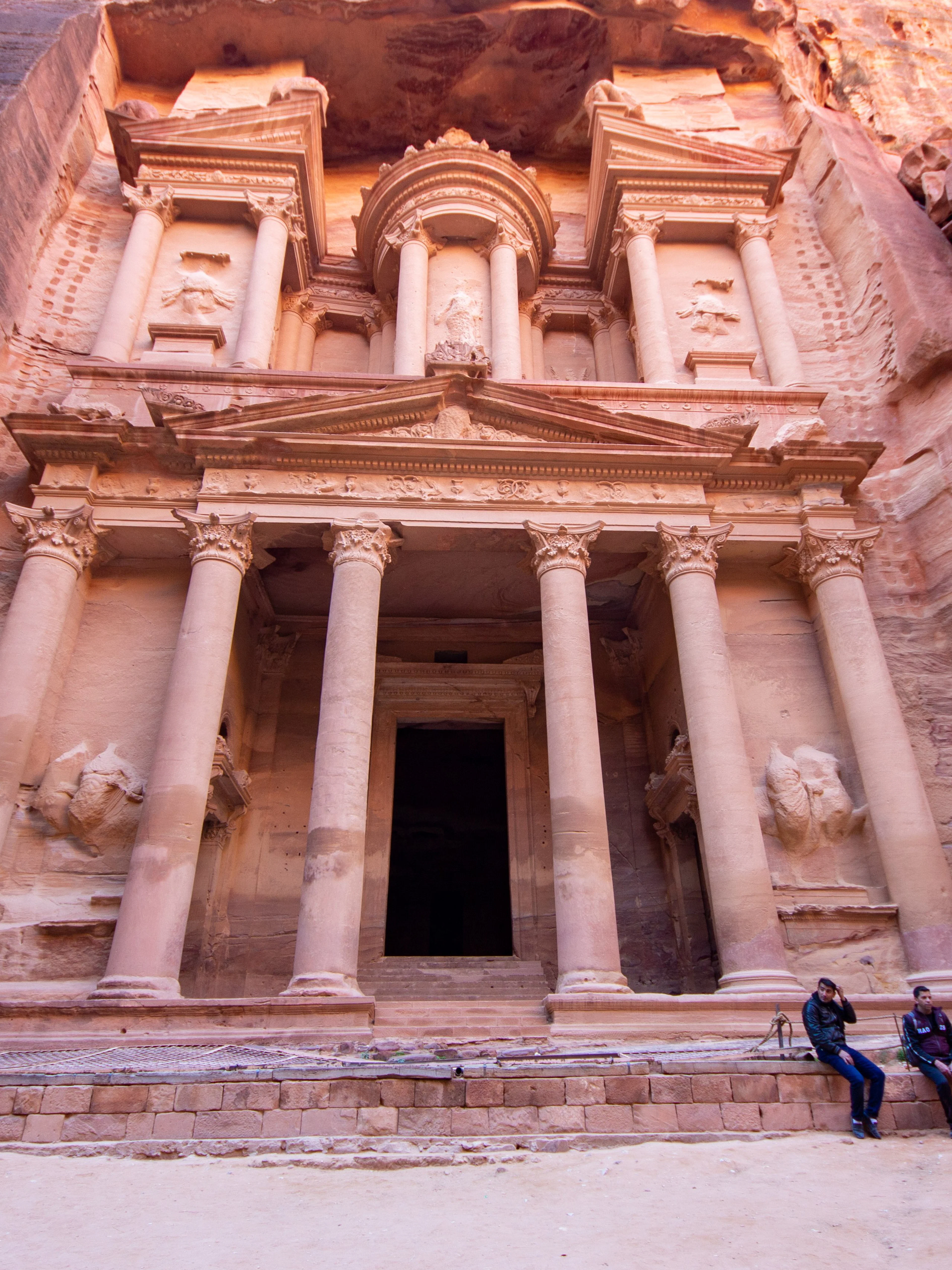 Petra's Al-Khazneh facade with visitors seated, Nabataean archaeological site, Jordan.