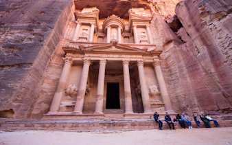 Petra's Al-Khazneh facade with visitors seated, Nabataean archaeological site, Jordan.