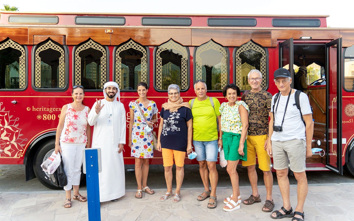 Tourists with a guide in front of a traditional red Dubai tour bus.