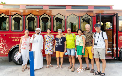 Tourists with a guide in front of a traditional red Dubai tour bus.