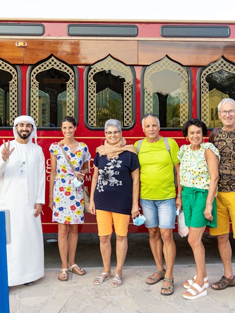 Tourists with a guide in front of a traditional red Dubai tour bus.