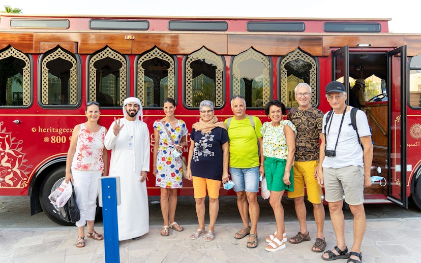 Tourists with a guide in front of a traditional red Dubai tour bus.