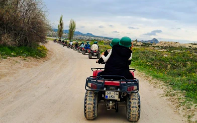 ATV riders on a dirt path with Cappadocia landscape in the background.