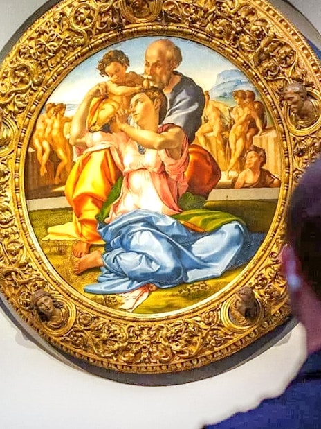 The Holy Family painting by Michelangelo at Uffizi Gallery, viewed by visitors.