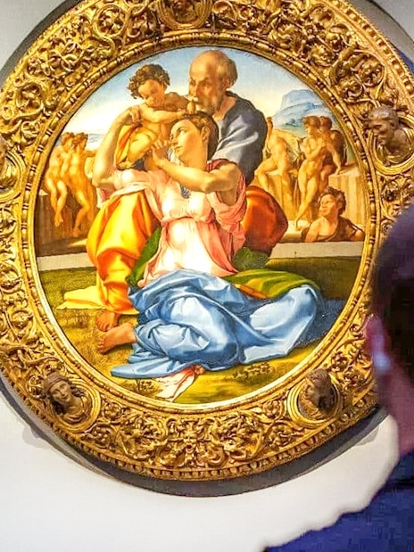 The Holy Family painting by Michelangelo at Uffizi Gallery, viewed by visitors.