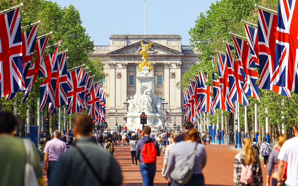Crowd walking towards Buckingham Palace, London, with Union Jack flags lining the path.