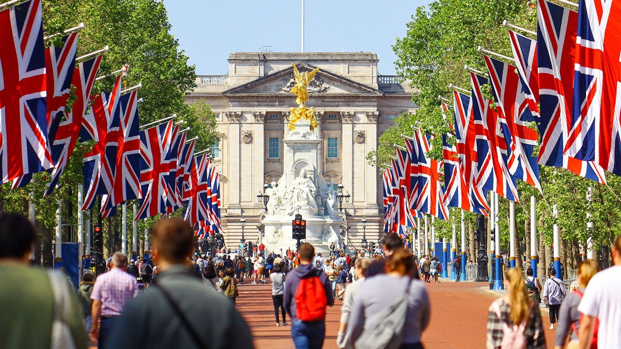 Crowd walking towards Buckingham Palace, London, with Union Jack flags lining the path.