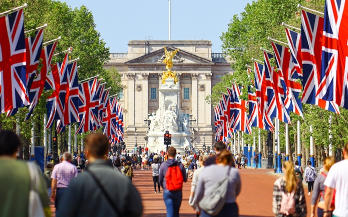 Crowd walking towards Buckingham Palace, London, with Union Jack flags lining the path.