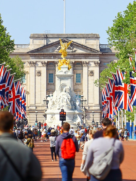 Crowd walking towards Buckingham Palace, London, with Union Jack flags lining the path.