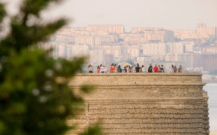 Tourists on Maiden Tower Museum rooftop, Baku, with city skyline in background.