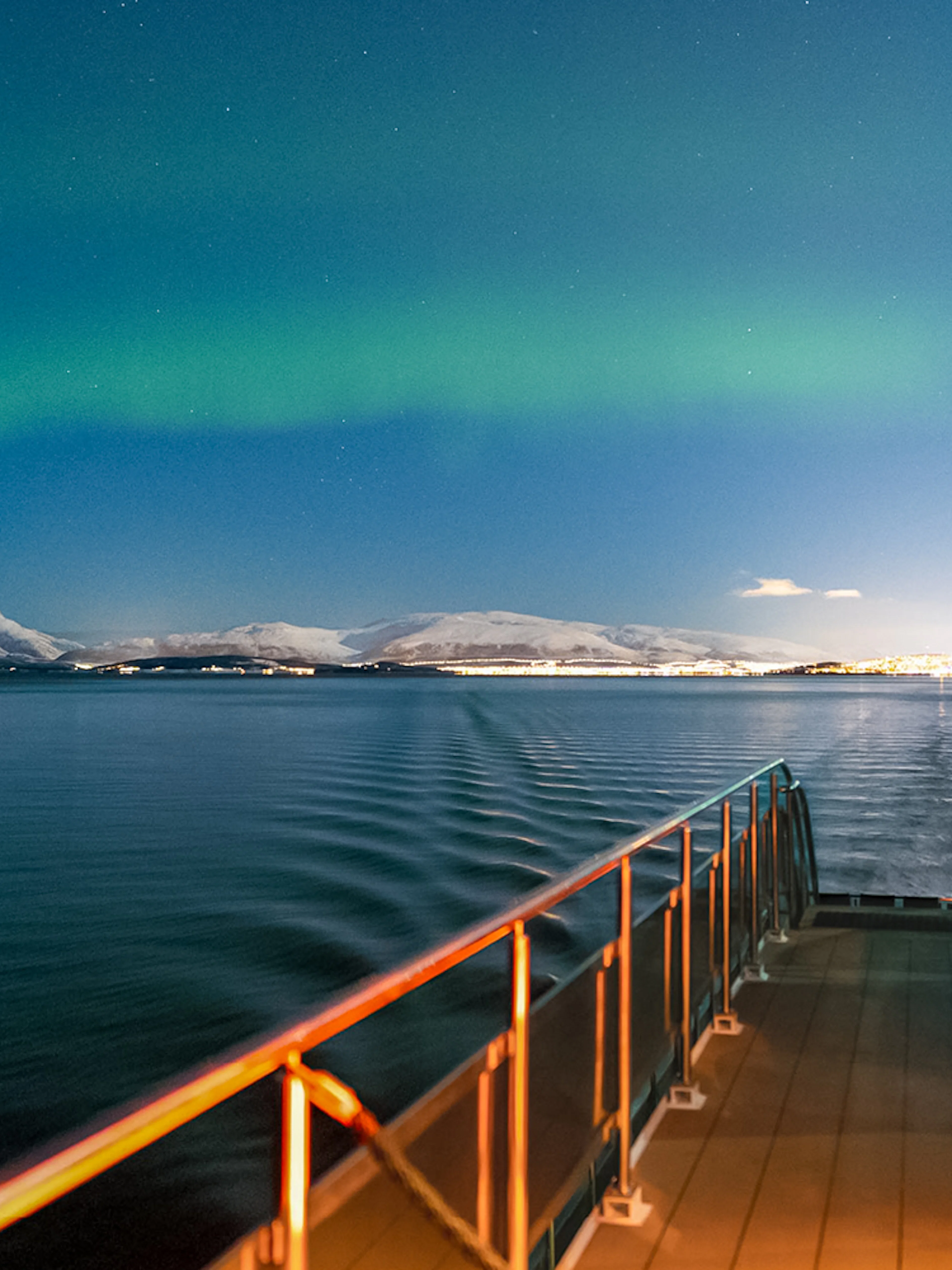 Cruise ship deck under Northern Lights with snowy mountains in the background.