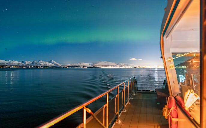 Cruise ship deck under Northern Lights with snowy mountains in the background.