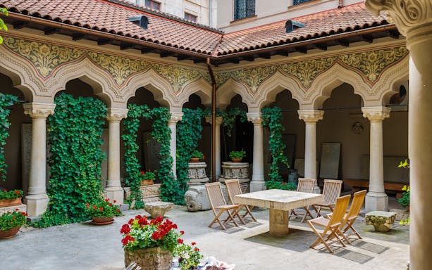 Courtyard with ornate arches and greenery in Bucharest, part of a walking tour and traditional lunch experience.