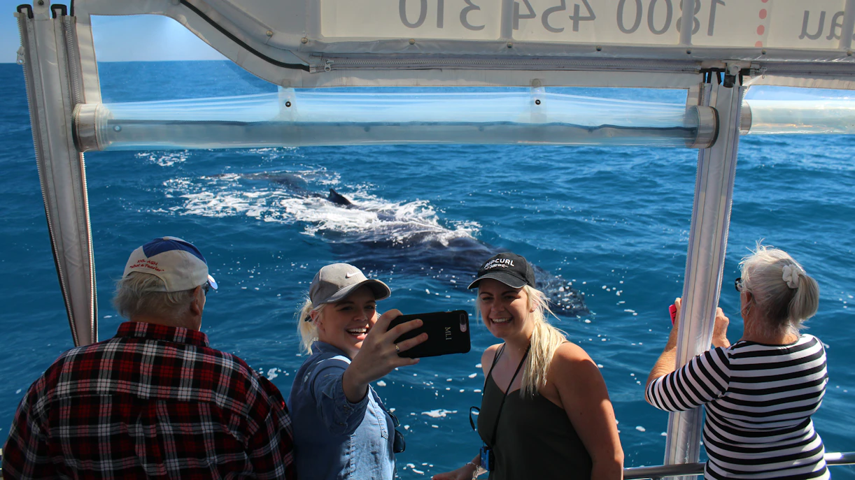 Two women take a selfie on a boat as a humpback whale swims by in Hervey Bay.